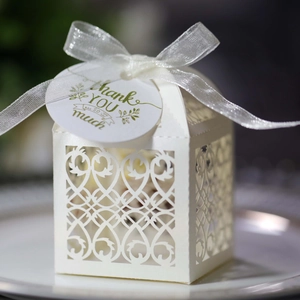 White laser-cut wedding favor box with vine patterns, white ribbon and thank you tag