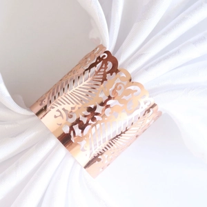Rose gold laser-cut vine napkin ring with hollow floral pattern on white linen fabric