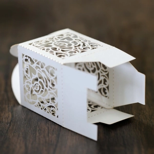 Detail of laser-cut rose patterns on white wedding candy boxes with wooden background