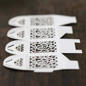 Macro shot of white laser-cut rose and lace patterns on flat paper wedding candy box