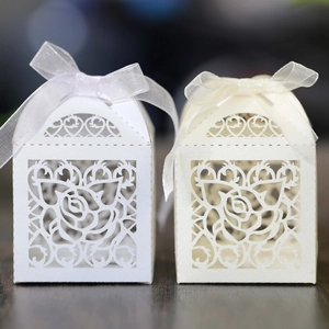 Detailed laser cut rose pattern on white and cream wedding candy boxes with satin ribbons