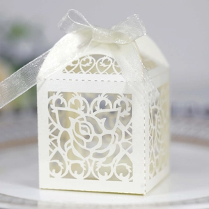 Macro shot of white laser-cut wedding favor box with rose patterns and organza ribbon