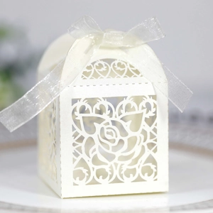 Detail of laser-cut ivory wedding favor box with rose patterns and silver silk ribbon