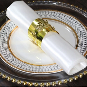 Elegant gold leaf napkin ring with intricate cutout design on a white satin napkin