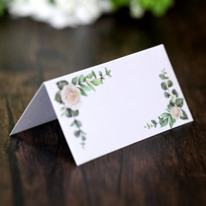Floral watercolor name place cards with white roses and eucalyptus on a wood table