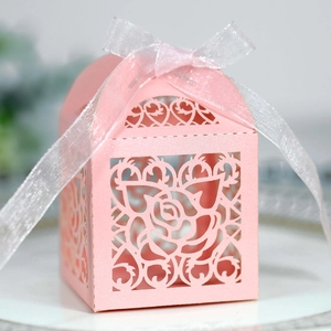 Close-up of pink laser-cut wedding favor box with rose patterns and white chiffon ribbon