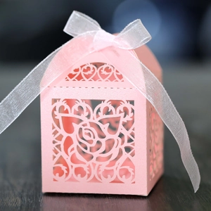 Close-up of pink laser-cut wedding favor box with rose patterns and white silk ribbon bow