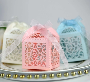 Detail of laser-cut rose hollow candy boxes with elegant satin ribbons for weddings