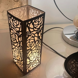 Black laser-cut metal candle holder with rose patterns and warm yellow LED lighting