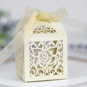 Detail of laser-cut rose patterns on cream wedding favor box with organza ribbon bow