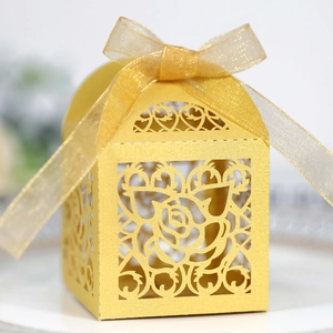 Macro view of gold laser-cut favor box with rose patterns and sheer ribbon bow