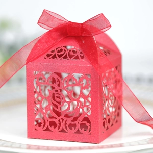 Close-up of red laser-cut wedding favor box with intricate rose patterns and silk ribbon