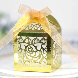 Macro view of gold laser-cut wedding favor box with intricate rose patterns and silk ribbon