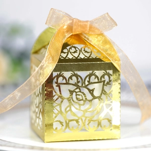 Detail of laser-cut rose patterns on a gold wedding favor box with organza ribbon bow