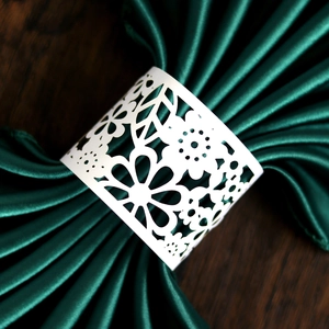 Laser-cut white floral paper napkin rings on dark green satin fabric for party decor