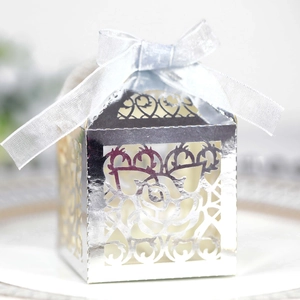 Close-up of laser-cut rose patterns on elegant silver wedding favor box with ribbon