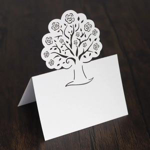 Elegant white laser-cut wedding place card with rose tree design on dark wood table