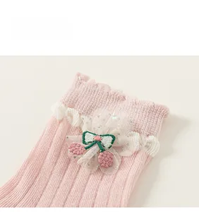 Détail de chaussettes roses pour enfants avec bordure à volants et broderie de cerises