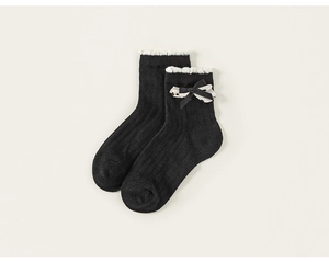 Détail de chaussette haute noire avec volant en dentelle blanche et nœud rayé élégant