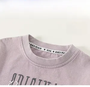 Détail macro du col rond violet avec ruban brodé Juicy Peach et finitions de qualité