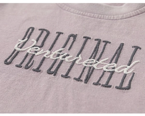 Détail de broderie multicouche et texture coton lavé sur un t-shirt violet pour enfant