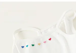 Gros plan de broderies de cœurs colorés sur un débardeur blanc en coton pour filles
