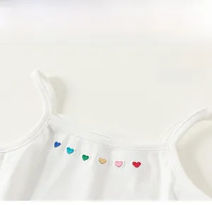 Détail d'un débardeur blanc pour fille avec six cœurs brodés colorés sur l'encolure du vêtement