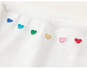 Gros plan sur tissu côtelé blanc avec six petits cœurs brodés colorés en ligne