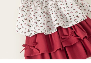 Detail of girls' floral top featuring red bow accents and ruffled hemline textures