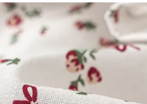 Detailed close-up of breathable floral cotton fabric with red berry pattern for girls clothing