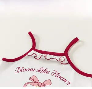 Détail d'un débardeur blanc fille avec bordure dentelle rouge et motif nœud rose