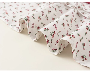 Close-up of floral fabric detail with red roses and small bows on off-white cotton dress