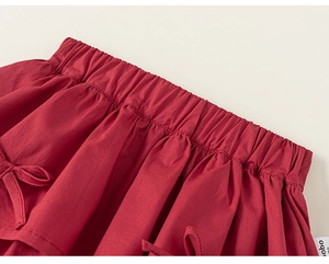 Detail view of red pleated cotton skirt featuring elastic waist and bow tie decoration