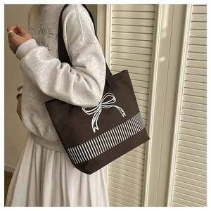Close-up of brown canvas tote bag featuring white bow graphic and stripe pattern