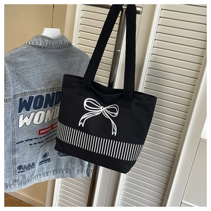 Detail of black canvas tote bag showing white hand-drawn bow and striped pattern