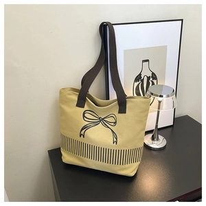 Detail view of khaki canvas tote with bow graphic and brown strap in modern studio setting