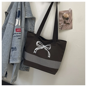 Detail of dark brown canvas tote bag featuring white bow print and striped design