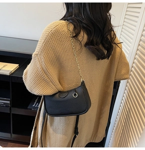 Close-up of black lychee grain leather underarm bag with gold chain strap on shoulder