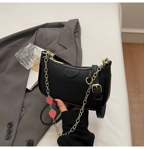 Detail of black lychee leather bag with gold chain and a red strawberry charm