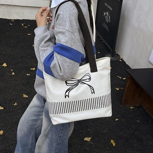 White canvas tote bag with black bow graphic and brown shoulder straps in casual street style