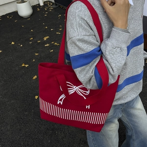 Red canvas tote bag with white bow print and dual straps shown in a stylish street setting