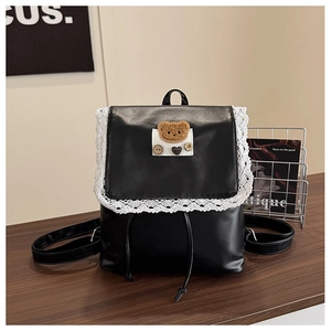 Detail of black leather backpack with lace trim and bear patch on dark wood surface