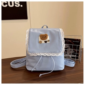 Detail of light blue PU leather backpack with lace trim and brown plush bear patch