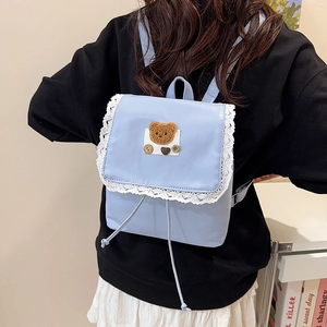 Sweet light blue backpack with white lace trim and a brown plush bear patch on a model