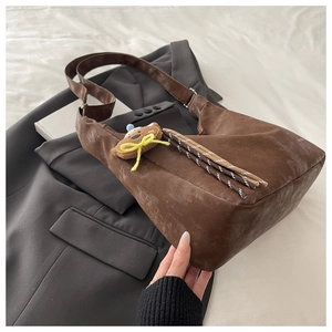 Detailed shot of brown suede shoulder bag with bear pendant on white bed linen