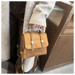 Close-up of caramel suede handbag showing three embossed bears and gold buckle detail