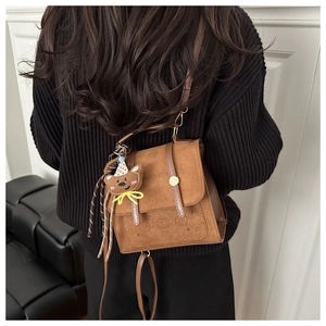 Close-up of brown faux leather backpack with bear pendant worn with black knitted sweater