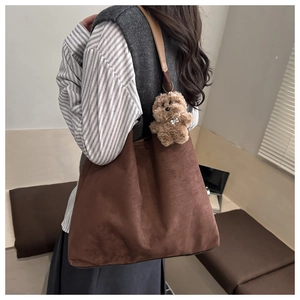 Detailed macro view of the dark brown matte suede texture and plush bear charm on tote bag