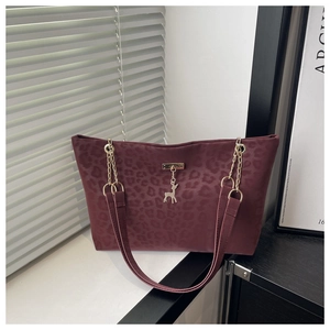 Detail of burgundy leopard print tote bag with gold chain strap and deer pendant charm