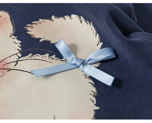 Dettaglio del top in maglia blu con stampa di cartoni e un fiocco decorativo in raso
